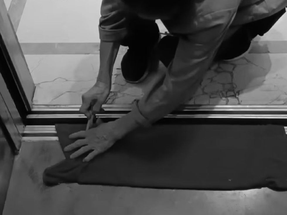 A black and white photo of a woman cleaning the floor of a lift