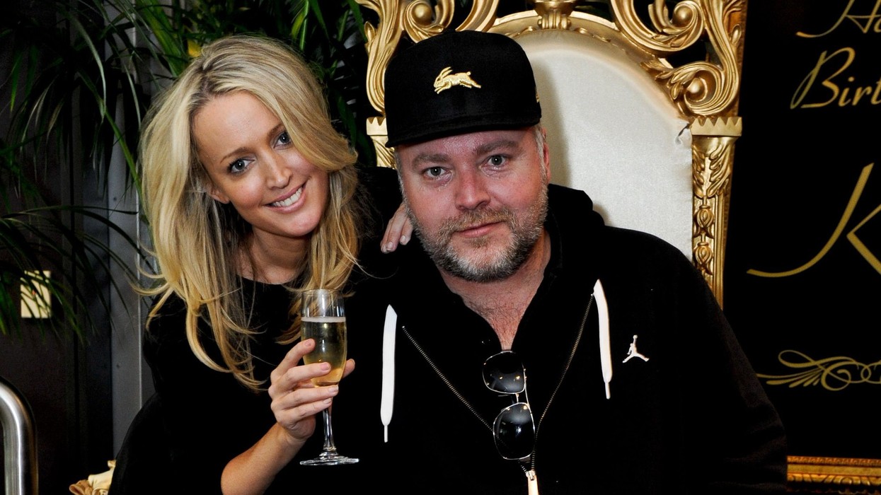 A blond haired woman with a glass of champagne stands next to a man wearing a baseball cap and track suit