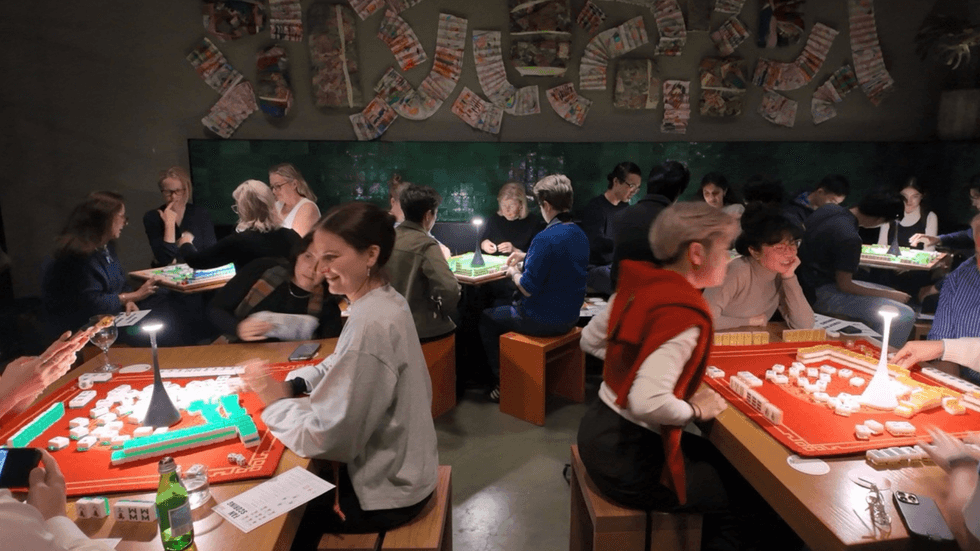 A busy mahjong games room with a number of tables filled with people