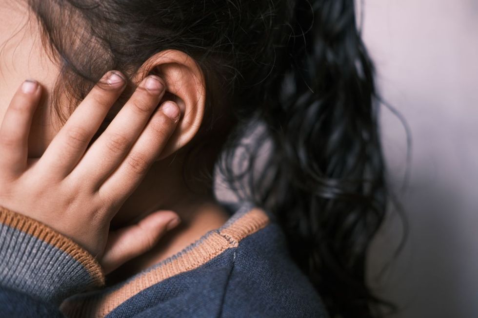 A child girl holding fingers up to her ear