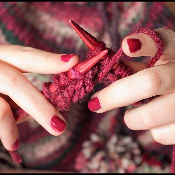 A close up of a woman's hands with red fingernails knitting a red jumper.