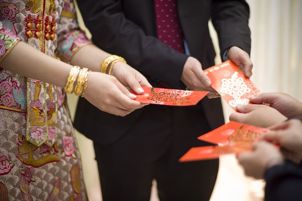 A couple dressed in traditional Chinese wedding outfits with red envelopes.