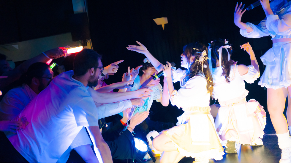 A crowd of mostly men reach for a group of young female performers