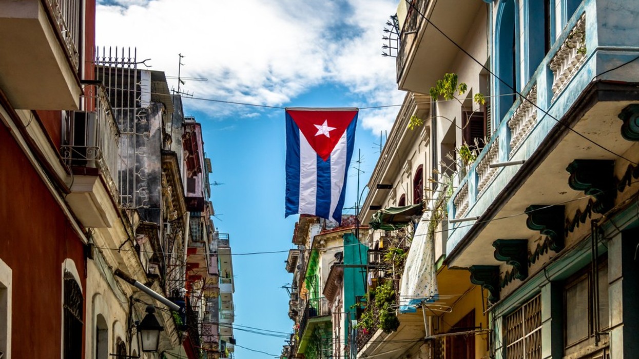A Cuban flag flies in a small street between houses with balconies.