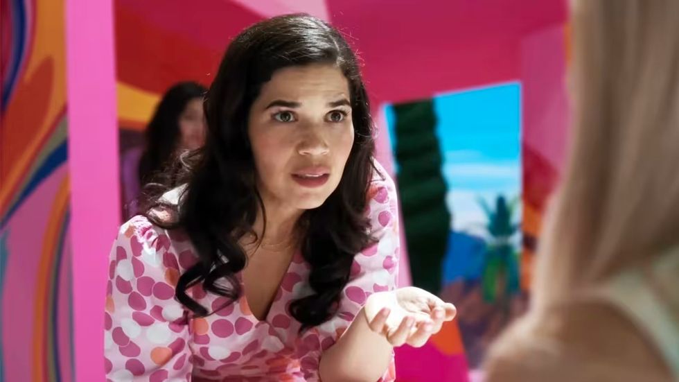 A dark haired woman in a pink outfit makes a speech.