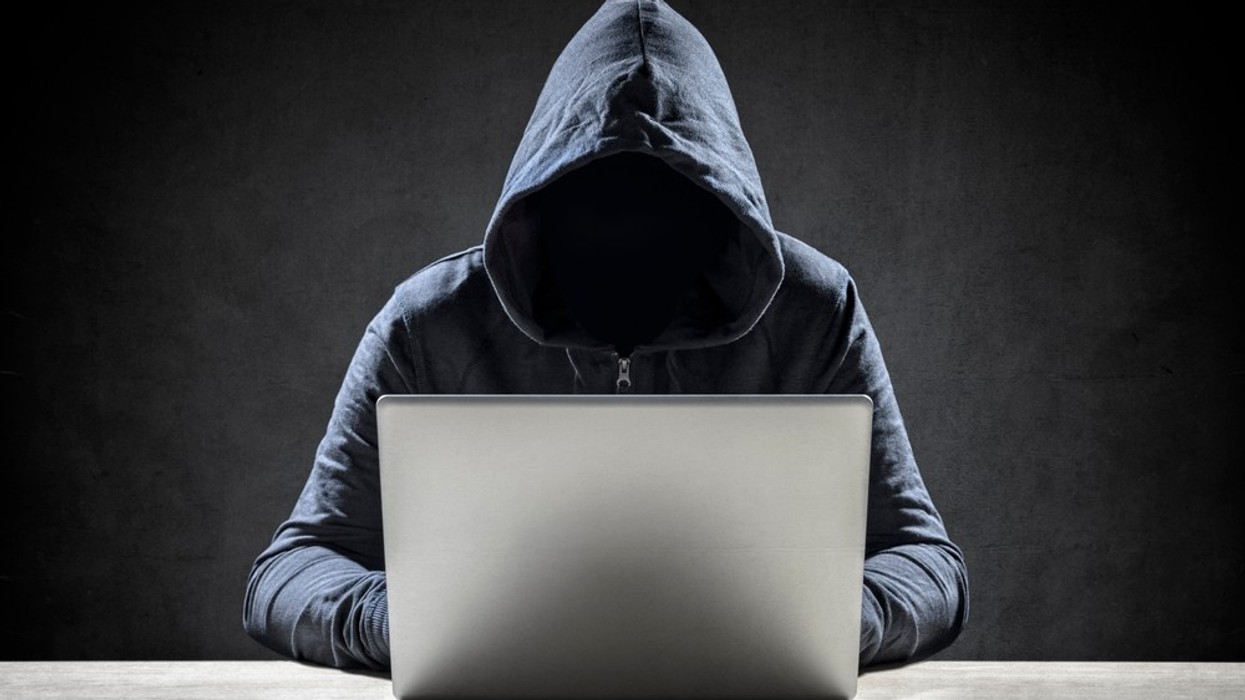 A faceless man in a hoodie on a laptop