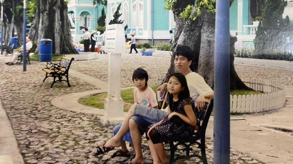 A father sits with his two children on a bench smiling at camera