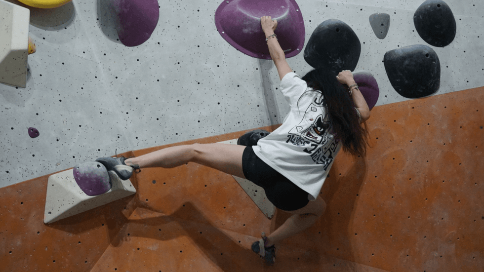 A female figure climbing a bouldering wall