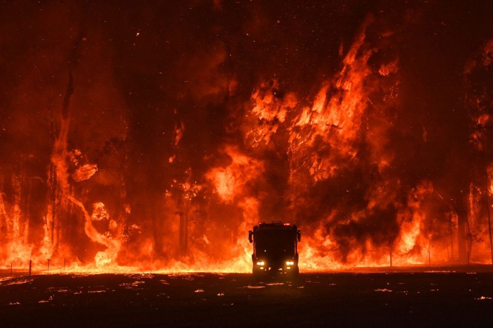 A fire crowning in the Australian bush. On the left is a fire tornado. In the centre is a firetruck with its headlights on.