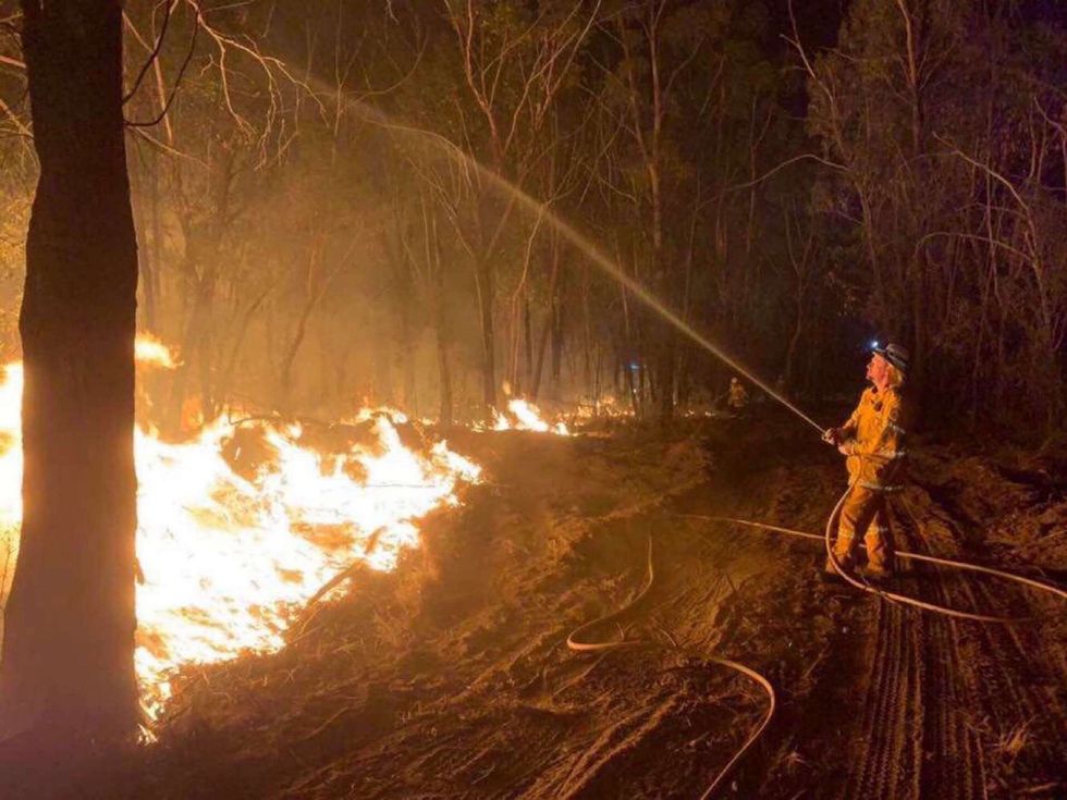 A firefighter holds a hose over a blaze