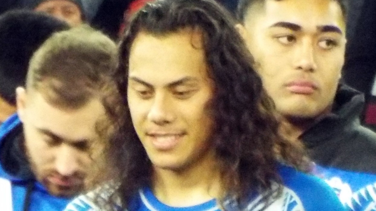 A football player with long hair at the end of a match stands with a child