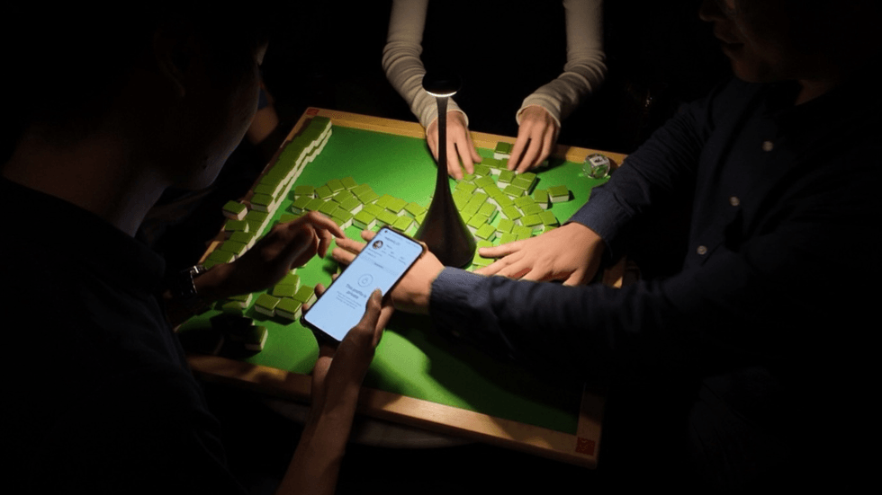 A green mahjong board with a man holding a phone showing instagram in the foreground