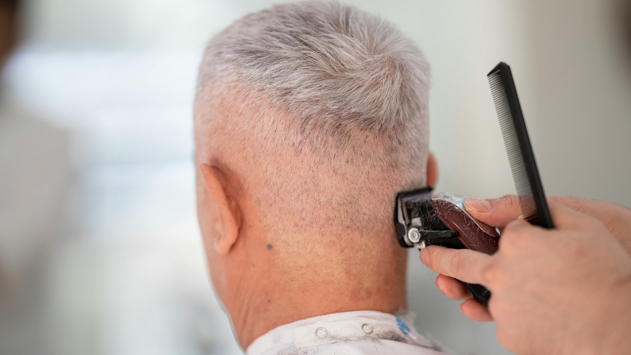 A grey haired man getting a hair cut