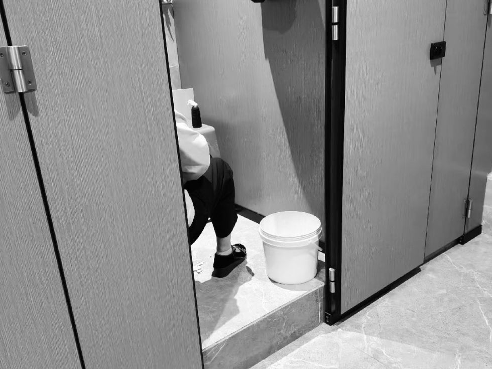 A hiddent figure sitting in a restroom cubicle