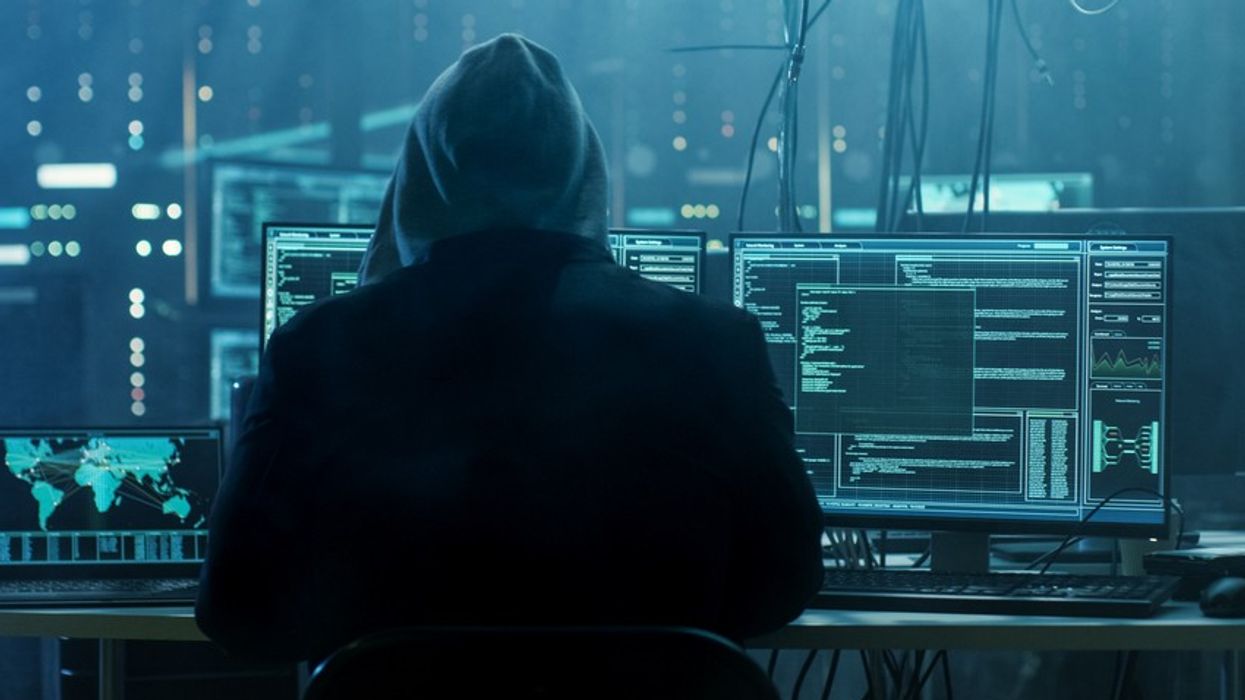 A hooded man sitting in front of screens