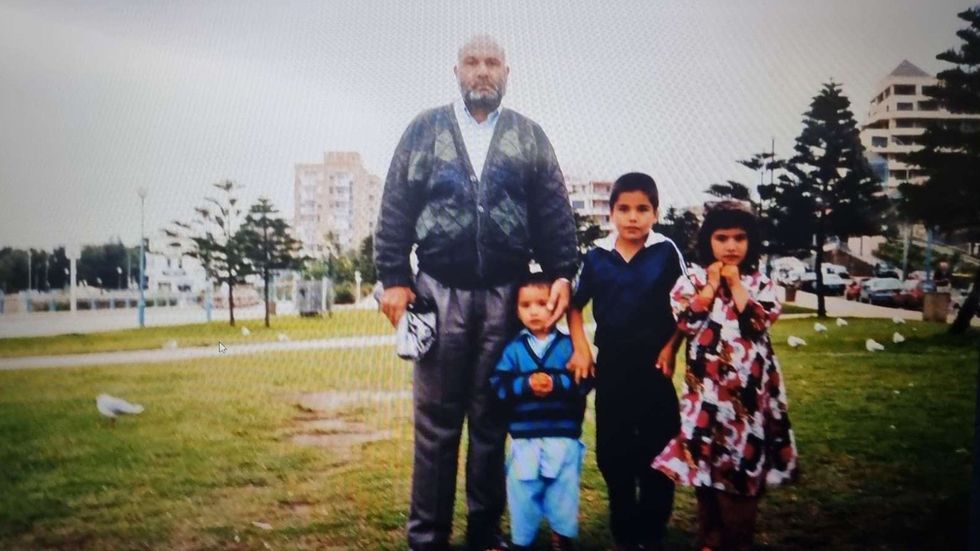 A man and three small children stand on the edge of a park.