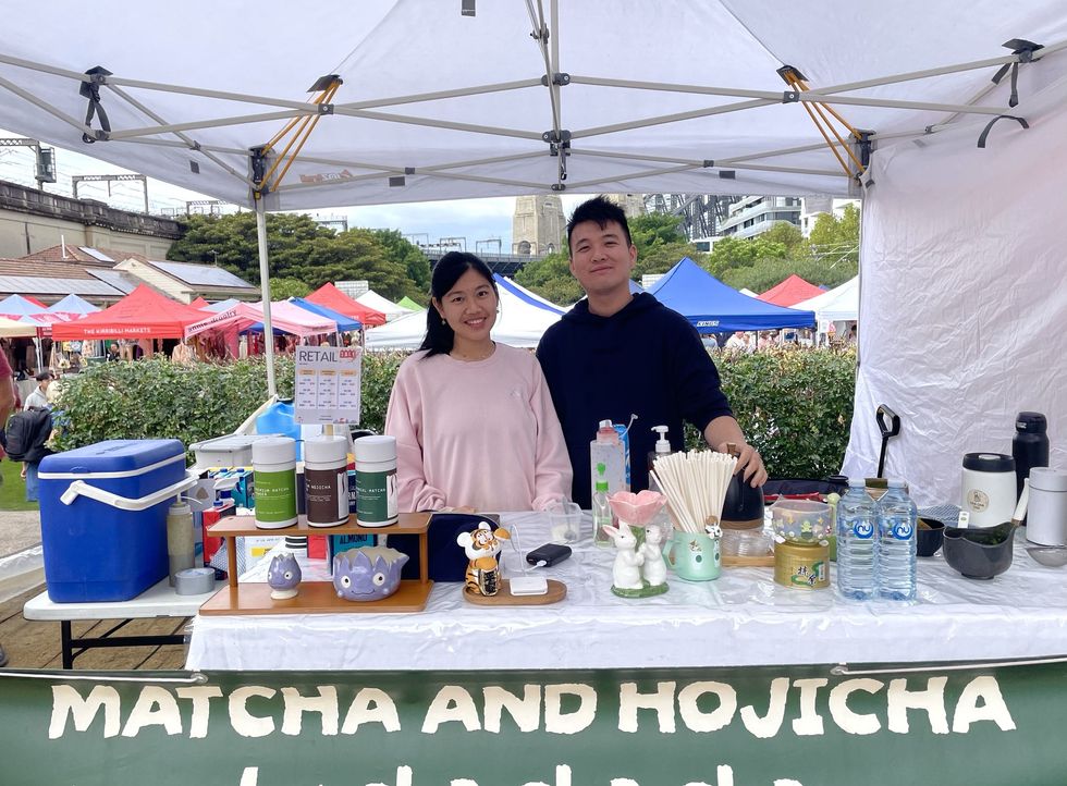 A man and woman standing behind a matcha stand at a market