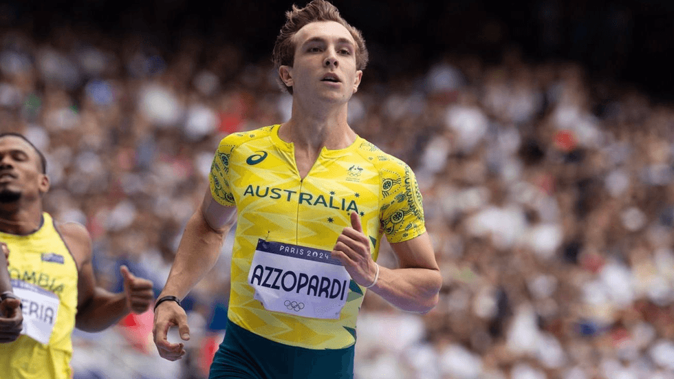 A man in a yellow top races on an athletics track