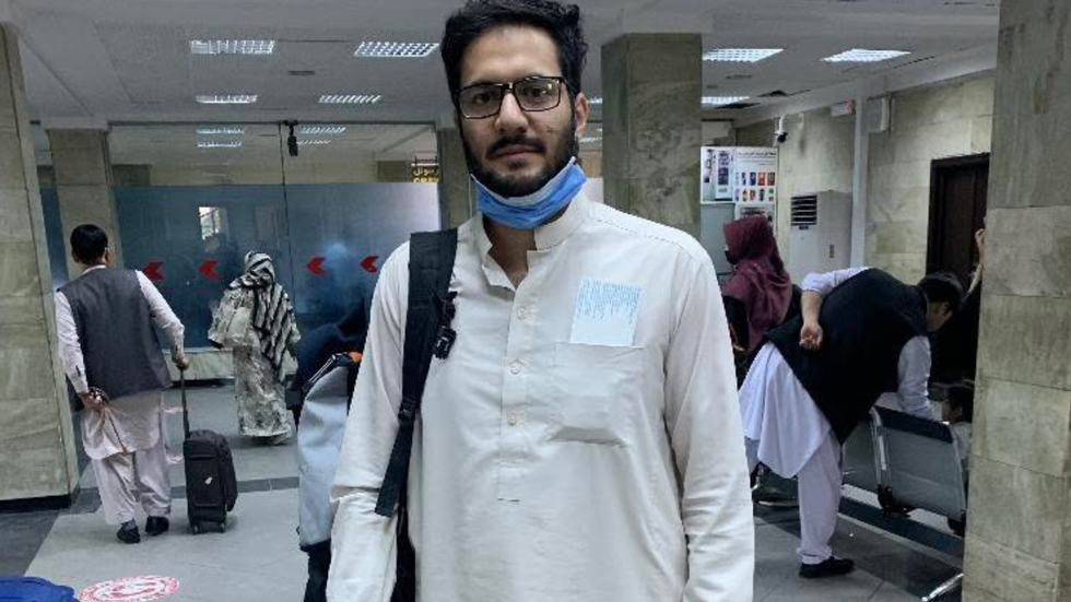A man in traditional dress with a mask and glass looks at the camera