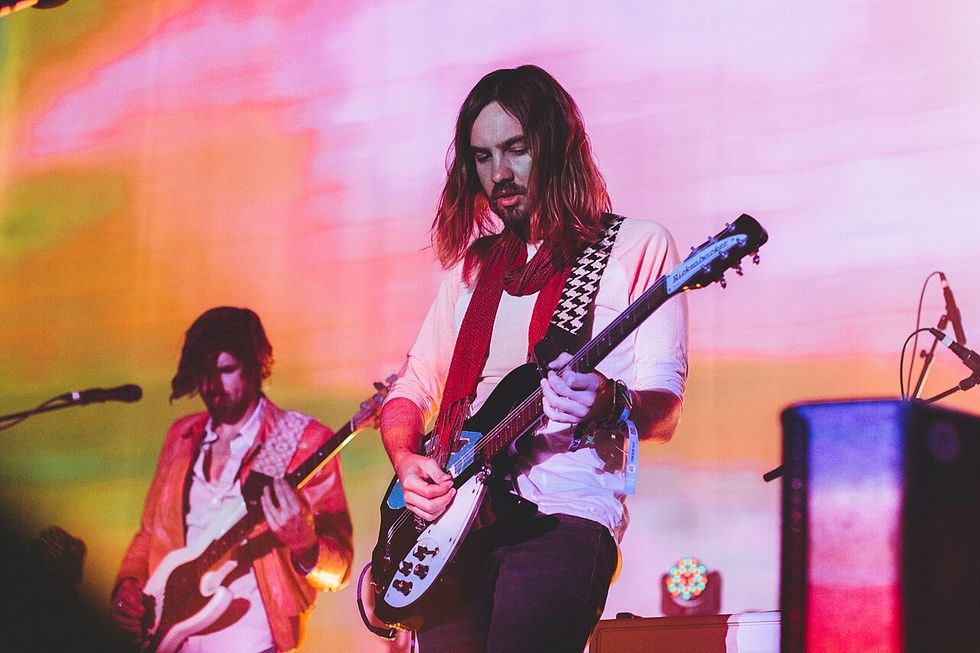 A man plays guitar against a multi coloured background