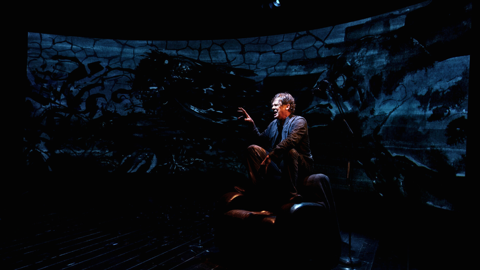 A man sits on a couch on a darkened stage
