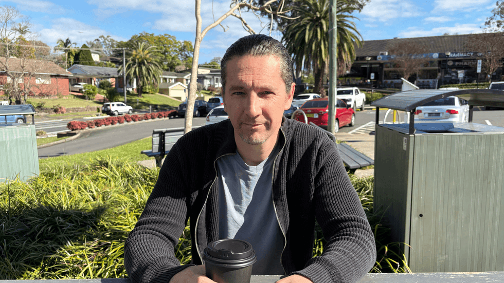 A man sitting on an outdoor bench with a coffee