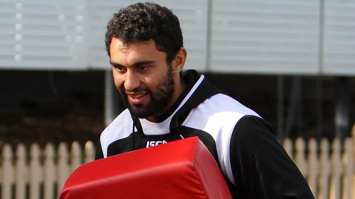 A man wearing a black and white tracksuit holds a red training bag