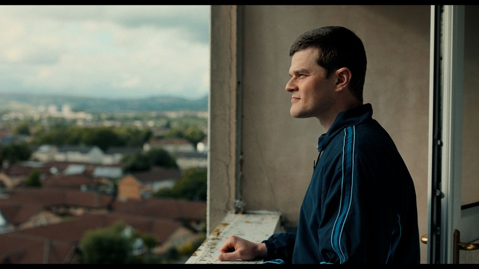 A man wearing a tracksuit stands on a balcony looking out at the view
