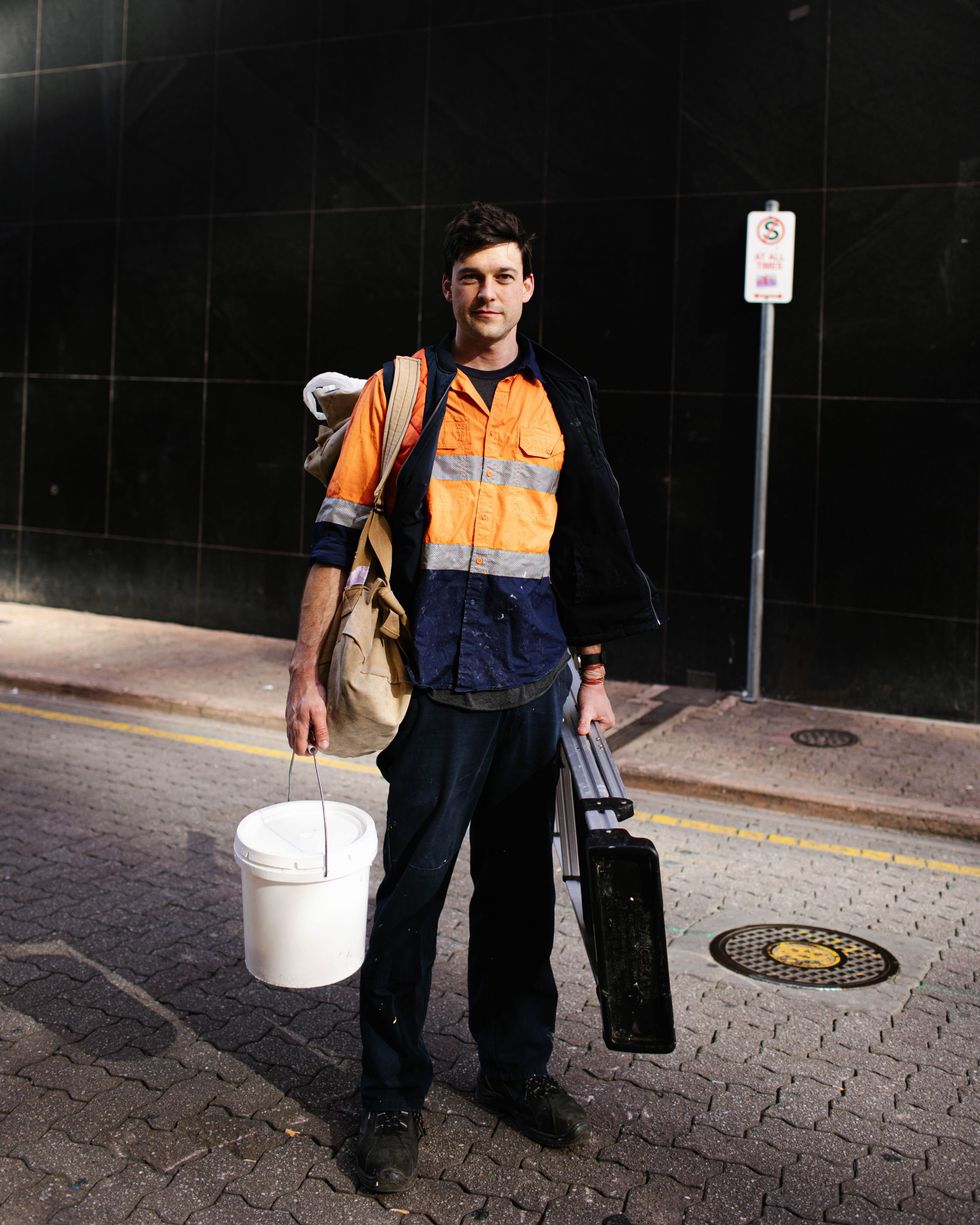 A man wearing fluoro clothes holding a bucket and a ladder smiles at the camera
