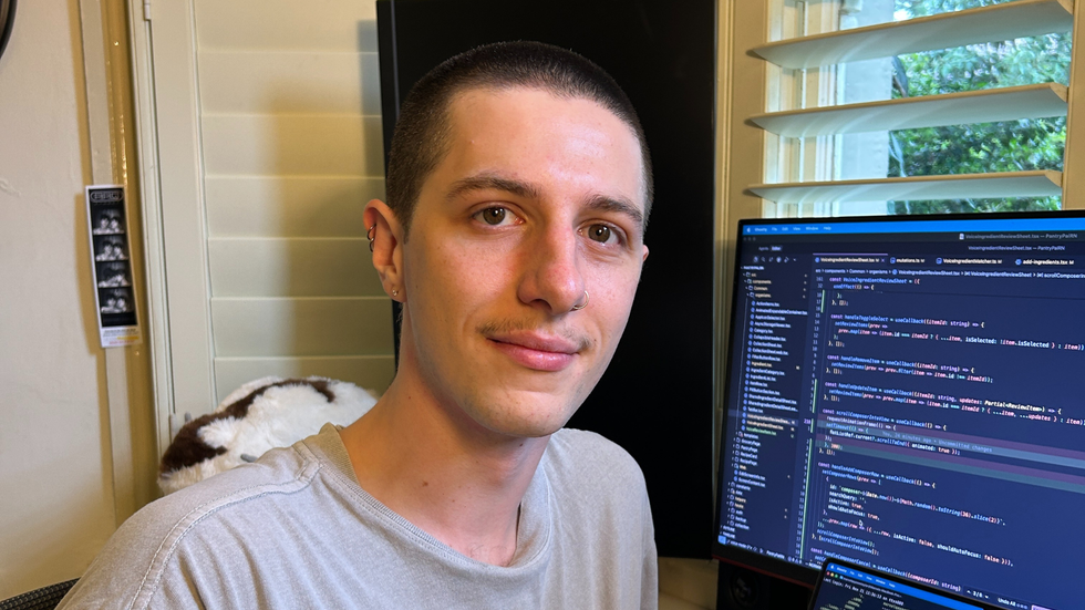 A man with a buzz cut sits in front of a computer screen showing code.