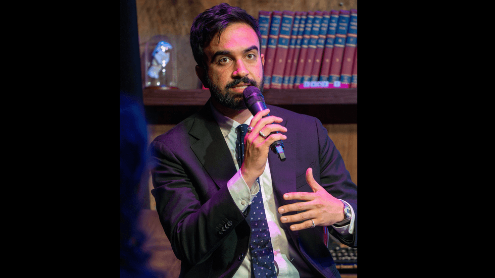 A man with dark hair in a suit holding a microphone