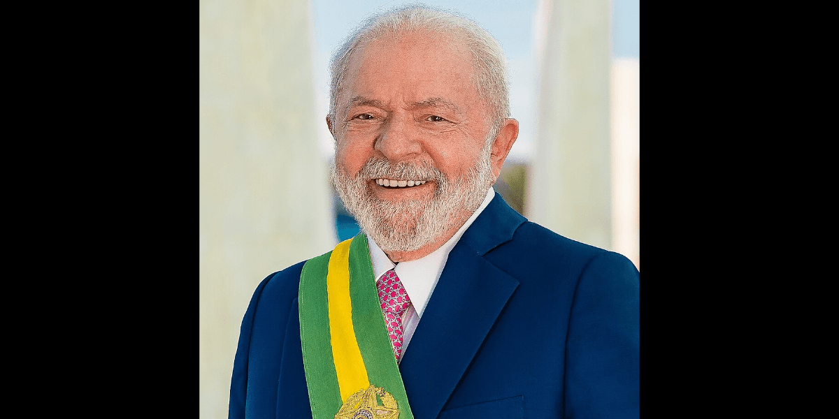 A man with grey hair in a navy suit and green sash