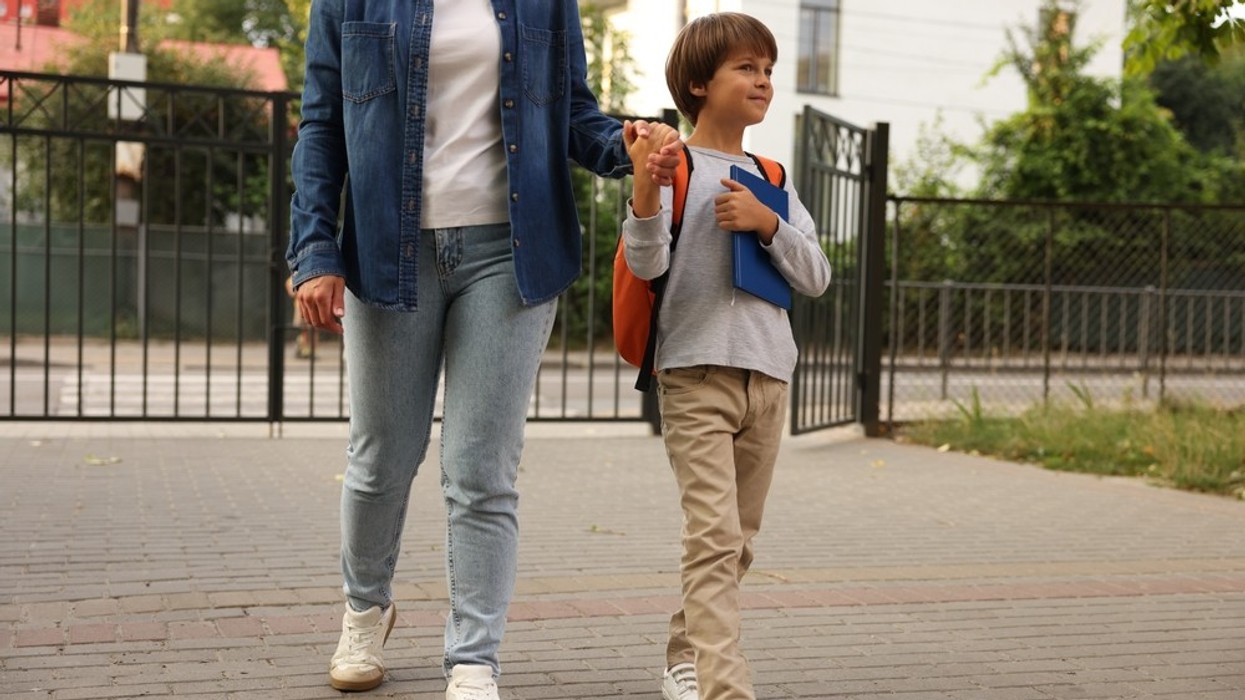 A mother holding her child's hand walking through the school gates.