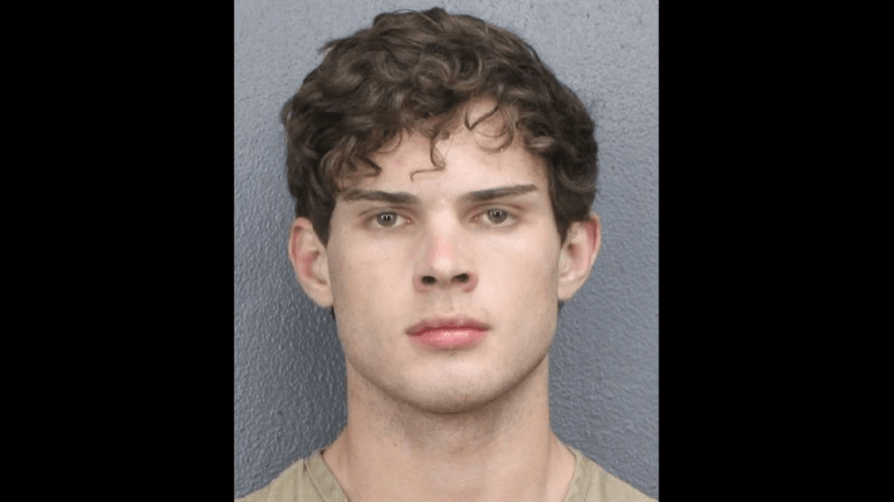 A mugshot of a young man with curly brown hair looks at the camera