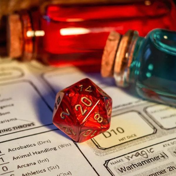 A multi-sided red die sits upon a character sheet for a Dungeons and Dragons game. Two bottles sit behind the die, one with blue liquid, the other with red.