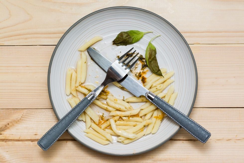 A plate with half eaten pasta and crossed knife and fork