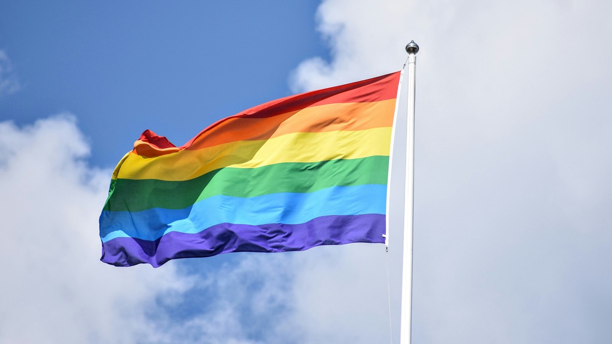 A rainbow flag flies from a flag post