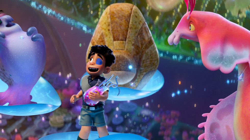 A screenshot from an animated film showing a small boy holding a cocktail glass. He's surrounded by multicoloured aliens.
