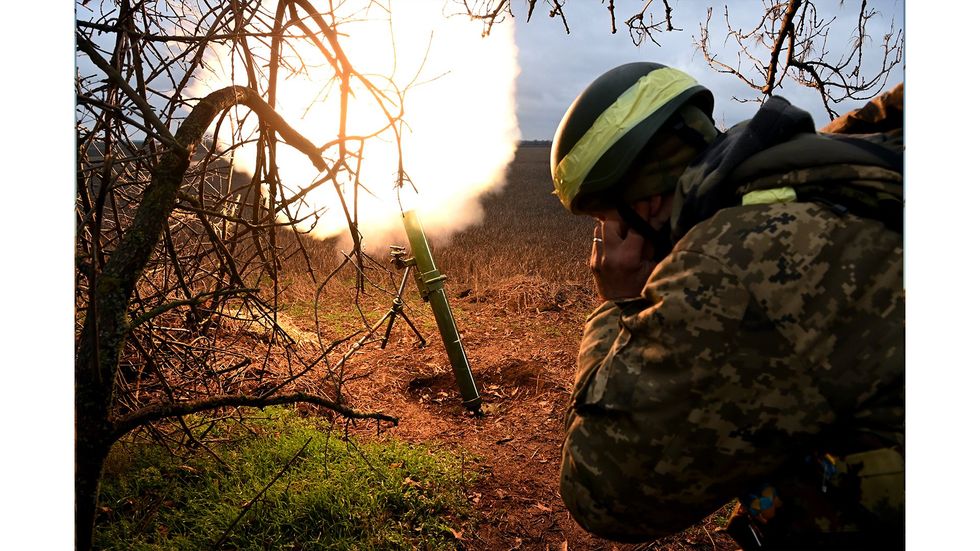 A Ukranian soldier blocks his ears as he fires a shell.