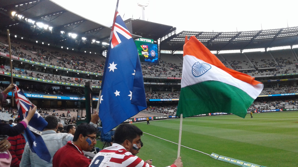 A view of a cricket ground with both Australian and Indian flags flying in foreground