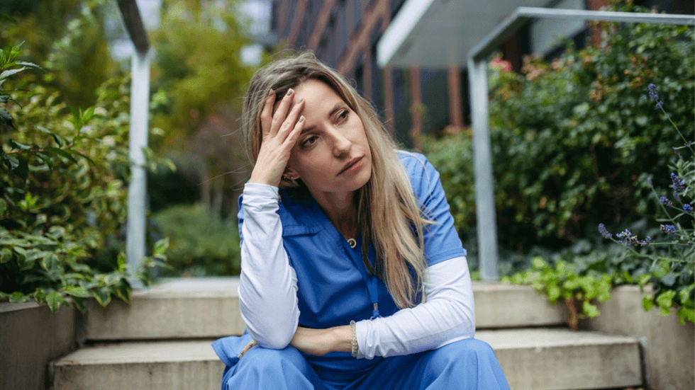 A woman in scrubs sitting on steps looking despairing