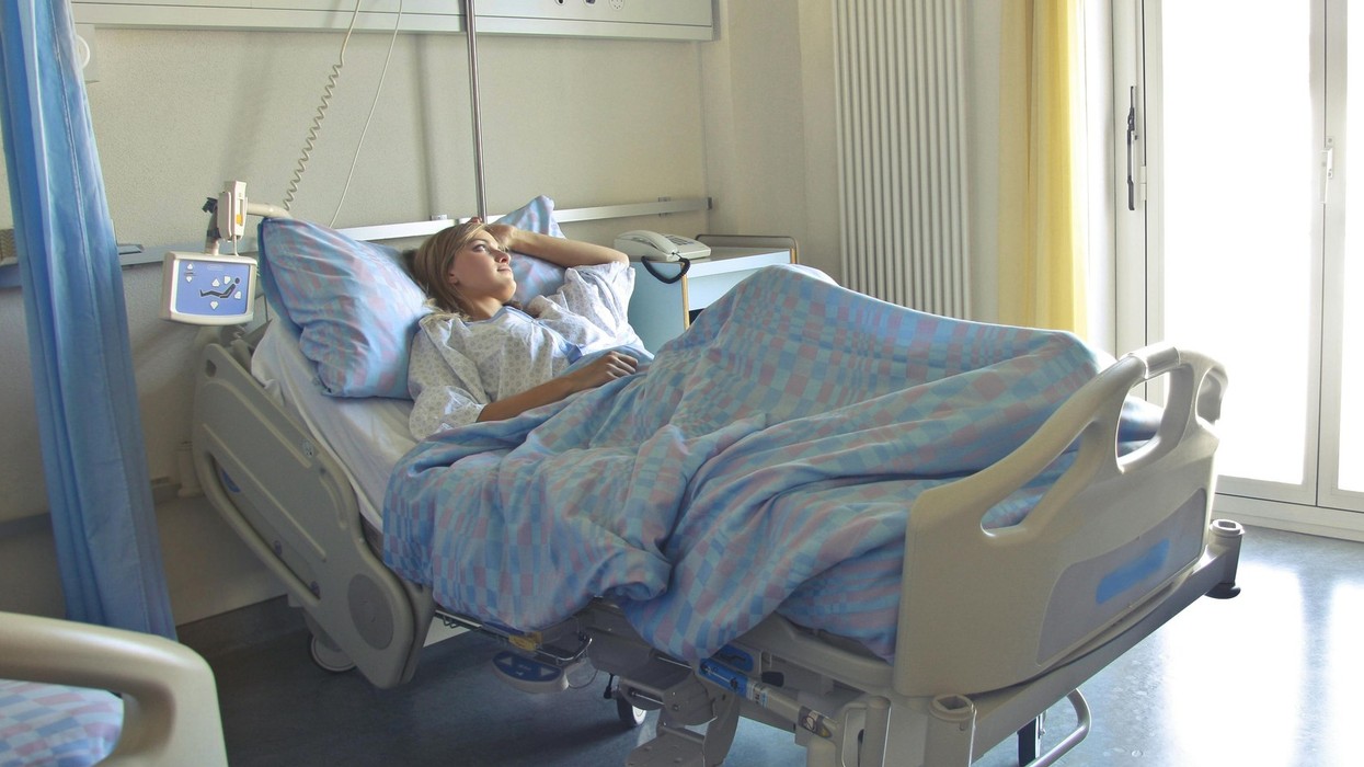 A woman lies in a hospital bed looking out the window