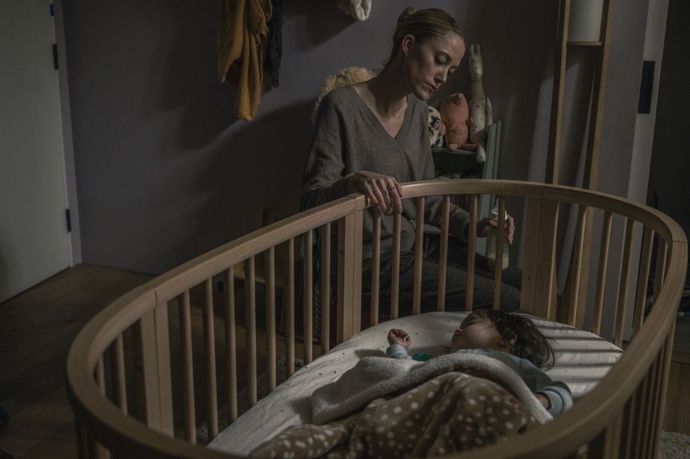 A woman looks at a baby sleeping in a cradle