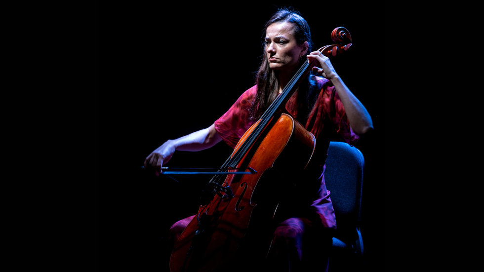 A woman playing a cello on a dark stage