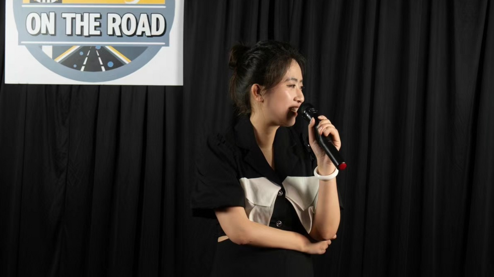 A woman sits on stage with a microphone, looking out to the audience