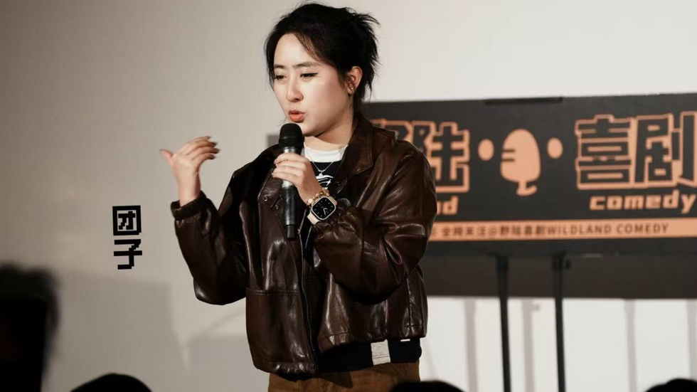 A woman sits on stage with a microphone, looking out to the audience
