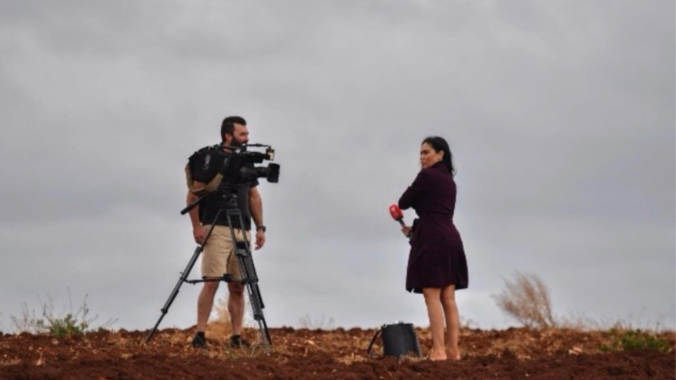 A woman stands opposite a camera and camera operator, out on location.
