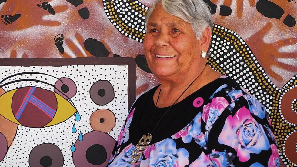 A woman wearing a colourful dress pictured in front of an Indigenous work of art