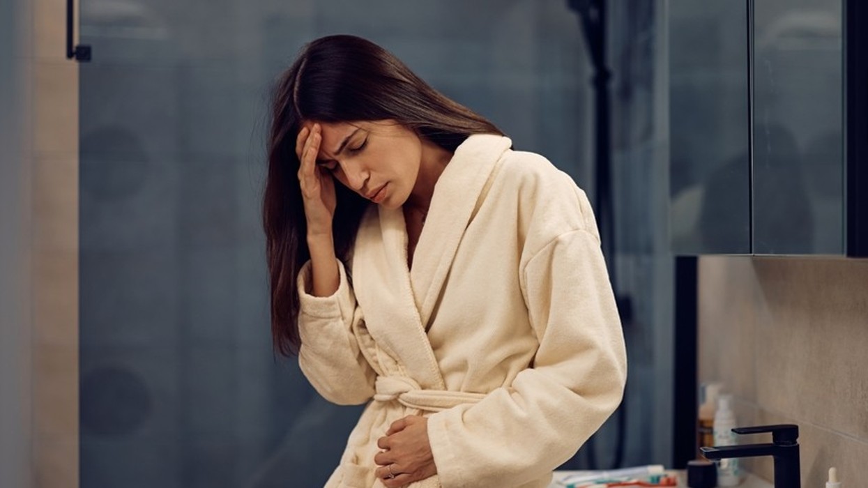 A woman wearing a dressing gown in a bathroom, looking like she's in pain