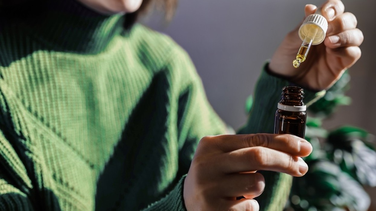 A woman with a green jumper holding a medicinal dropper and a small jar